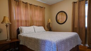 A neatly made bed with a patterned bedspread, two bedside lamps, a round mirror on the wall, and a wooden nightstand with a lamp. - Charming home near Boise State and The Train Depot
 (Boise)