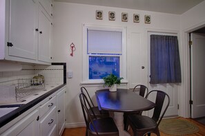 A dining area with a table and chairs, a window with blinds, and a door with a checkered curtain.