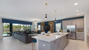 A modern kitchen with a central island, stainless steel appliances, and a dining area with a pool view. - Premium Home w Princess & Superhero BRs, Theater, Game Loft, Pool - Mins to Disn (Kissimmee)