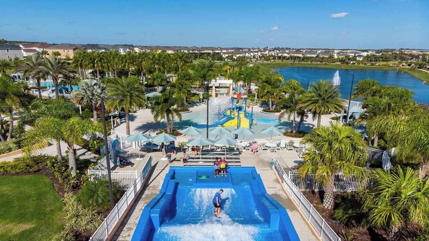 A water park with a large pool, palm trees, and a view of a lake. - Premium Home w Princess & Superhero BRs, Theater, Game Loft, Pool - Mins to Disn (Kissimmee)