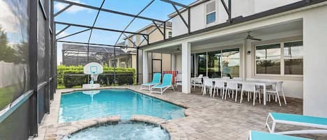 An indoor swimming pool with a hot tub, surrounded by lounge chairs and a dining area with tables and chairs.