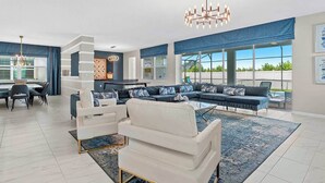 A spacious living room with a large sectional sofa, a dining area with a glass table, and a kitchen in the background. - Premium Home w Princess & Superhero BRs, Theater, Game Loft, Pool - Mins to Disn (Kissimmee)
