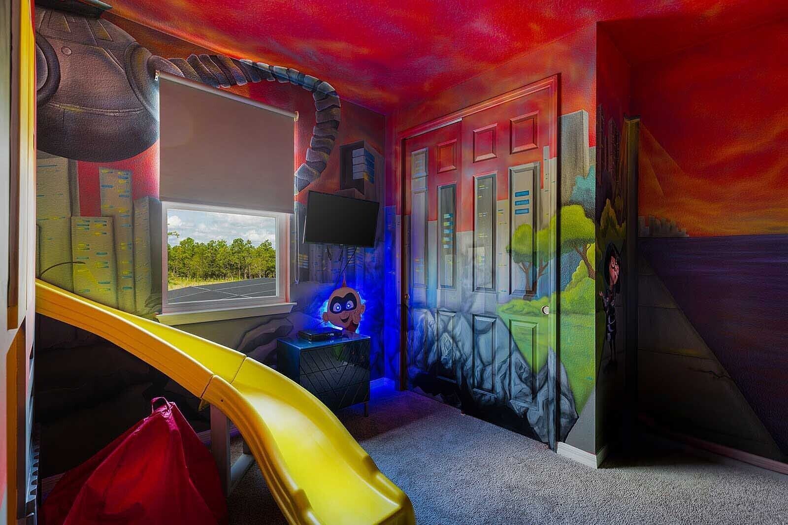 Een kamer met een raam, een bureau, een stoel en een kleurrijke muurschildering.