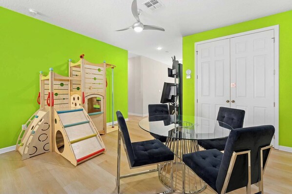 A room with a play area, a glass table with chairs, and a white door.