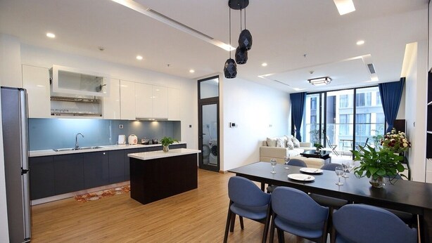 A modern kitchen with a central island, a dining area with a table and chairs, and a living space with a sofa and a coffee table. - 3 bedroom in Metropolis near Lotte, Dao Tan (Hanoi)