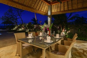 Enjoy a meal under the shade of a thatched roof, surrounded by lush vegetation and a serene pool.