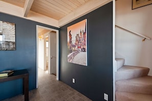 A hallway with a dark wall, a wooden ceiling, and a staircase with beige carpet.