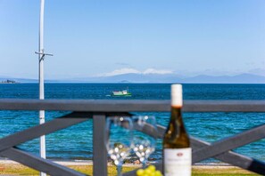 A coastal view with a boat on the water, a bottle of wine, and a glass on a balcony railing.