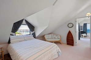 Ein Schlafzimmer mit einem großen Bett, einem fenster mit Vorhängen, einem Sessel, einer Uhr und Meerblick.