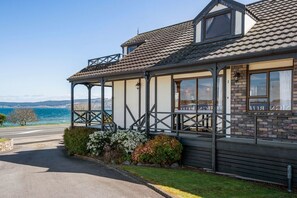 A coastal building with a balcony, a view of the sea, and a paved driveway.