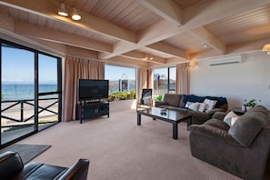 Ein großzügiges Wohnzimmer mit großem Fernseher, bequemen Sitzmöglichkeiten und Blick auf das Meer.