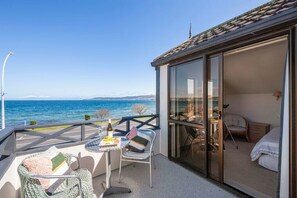 A balcony with a table set for two, a chair, and a view of the sea.
