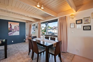 A dining area with a wooden table and chairs, a window with curtains, and framed pictures on the wall.
