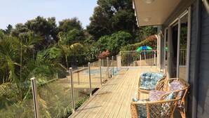 A wooden deck with wicker chairs and a glass railing overlooking a swimming pool and lush greenery. - Incredible harbour views, secluded four bedroom character villa, private drive (Whangaroa)