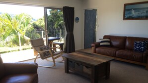 A living room with a brown leather sofa, a rocking chair, a wooden coffee table, and a view of a balcony with palm trees. - Incredible harbour views, secluded four bedroom character villa, private drive (Whangaroa)