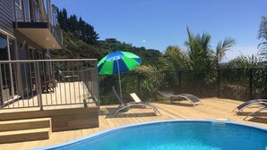 A swimming pool with lounge chairs and an umbrella, surrounded by a wooden deck and a metal fence. - Incredible harbour views, secluded four bedroom character villa, private drive (Whangaroa)