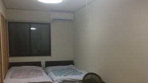 A small, dimly lit room with two beds, a window, and a chair. - Near JR AWAJI station <br> 30 min. to Kyoto .10 min. to umeda.<br> 40 min.<br> (Osaka city higashiyodogawa ku)