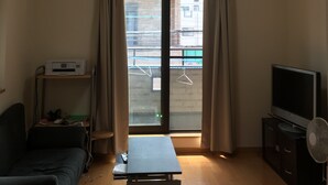 A living room with a sofa, a table, a TV, and an air conditioning unit. - Near JR AWAJI station <br> 30 min. to Kyoto .10 min. to umeda.<br> 40 min.<br> (Osaka city higashiyodogawa ku)