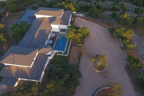 An aerial view of a modern house with a swimming pool, a covered patio, and a driveway. - 9000 Sqft Estate/Pickleball/Basketball/Pool/HotTub/9 Bdrm/8 Bath/23Beds/Sleeps35 (Dripping Springs)