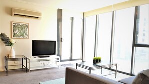 A modern living room with a flat-screen TV, a sofa, a coffee table, and a large window offering a city view. - In the heart of Southbank! (Southbank)