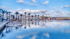 Un hôtel situé au bord de l’eau, doté d’une piscine dont l’eau reflète les bâtiments et les palmiers.
