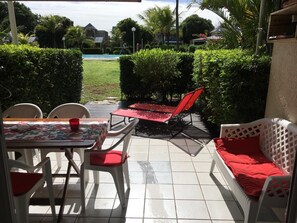 Un'area patio con tavolo, sedie, barbecue e divano con cuscini rossi.