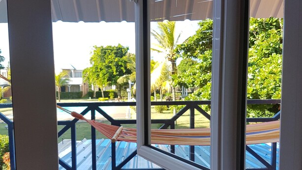 A window with a view of a pool area, including a hammock and a railing.