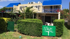 A two-story building with a blue roof, a balcony with blue railings, and a green sign with a white tree design.