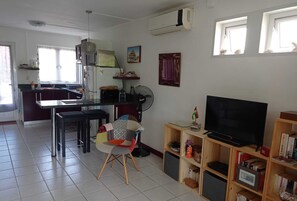 A living room with a TV, bookshelves, a fan, and a dining area with a table and chairs.