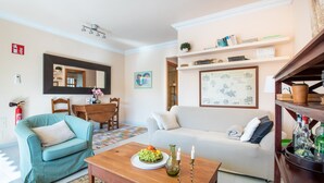 A living room with a sofa, a coffee table with fruit and candles, a teal armchair, a wooden dining table, and a bookshelf. - Apartment Carla near the beach with spacious balcony, mountain view, Wi-Fi & air conditioning (Puerto de Soller)