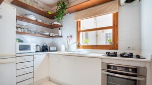 A kitchen with white cabinets, a microwave, a stove, and a window with a view. - Apartment Carla near the beach with spacious balcony, mountain view, Wi-Fi & air conditioning (Puerto de Soller)