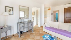 A living room with a white sofa, a grey console table with decorative items, a large mirror, and a tiled floor. - 4 km from Porto Cervo with panoramic terrace (Abbiadori)