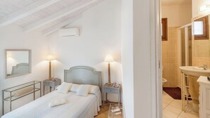 A bedroom with a bed, bedside tables, lamps, and a bathroom with a sink and mirror. - 4 km from Porto Cervo with panoramic terrace (Abbiadori)
