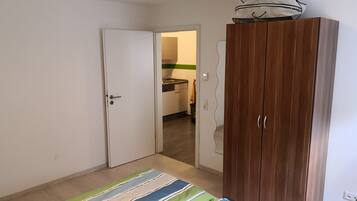 A room with a wooden wardrobe, a striped rug, and a door leading to a kitchen.