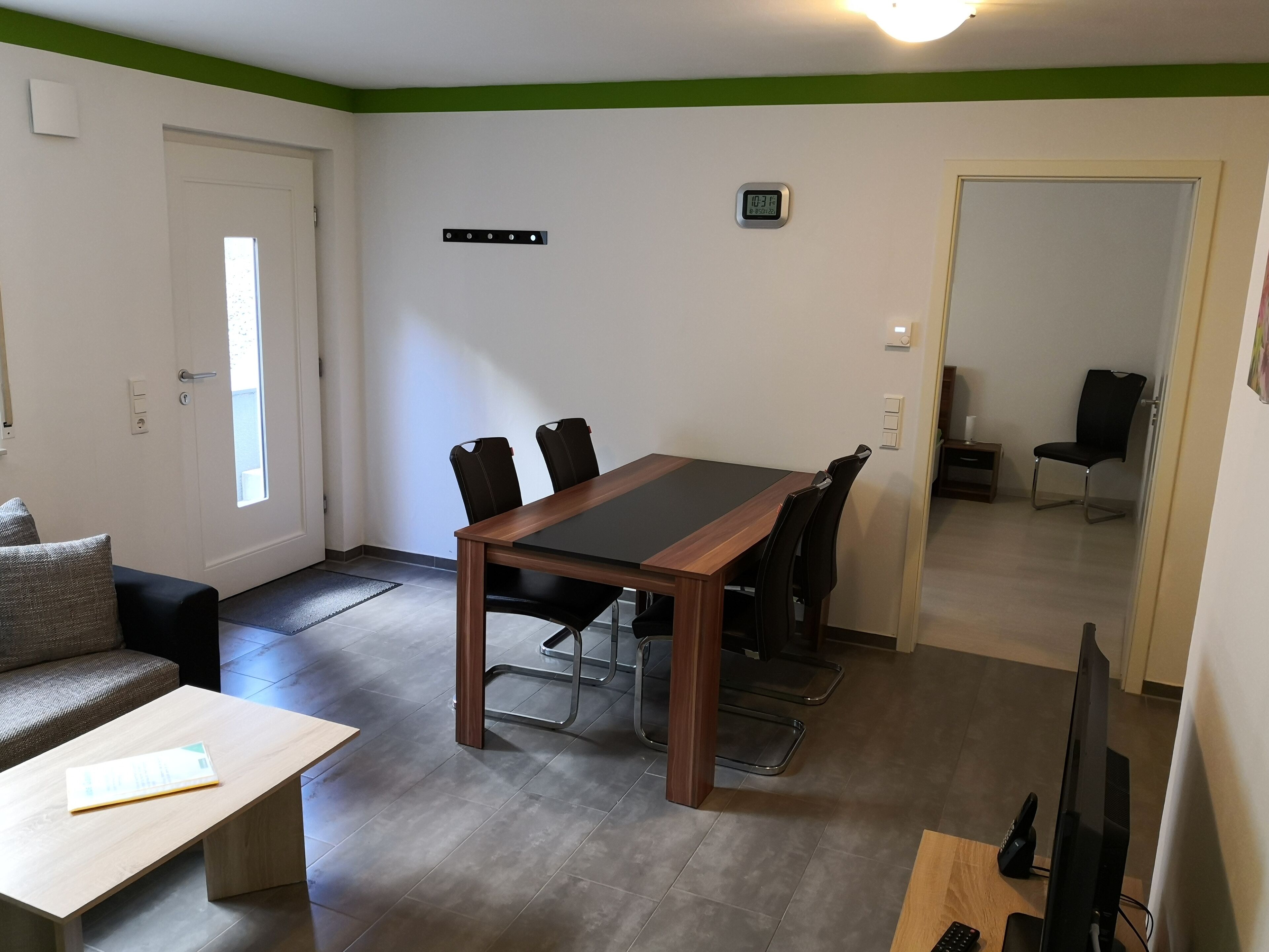 A modern living room with a wooden dining table, black chairs, a grey sofa, and a small wooden coffee table.