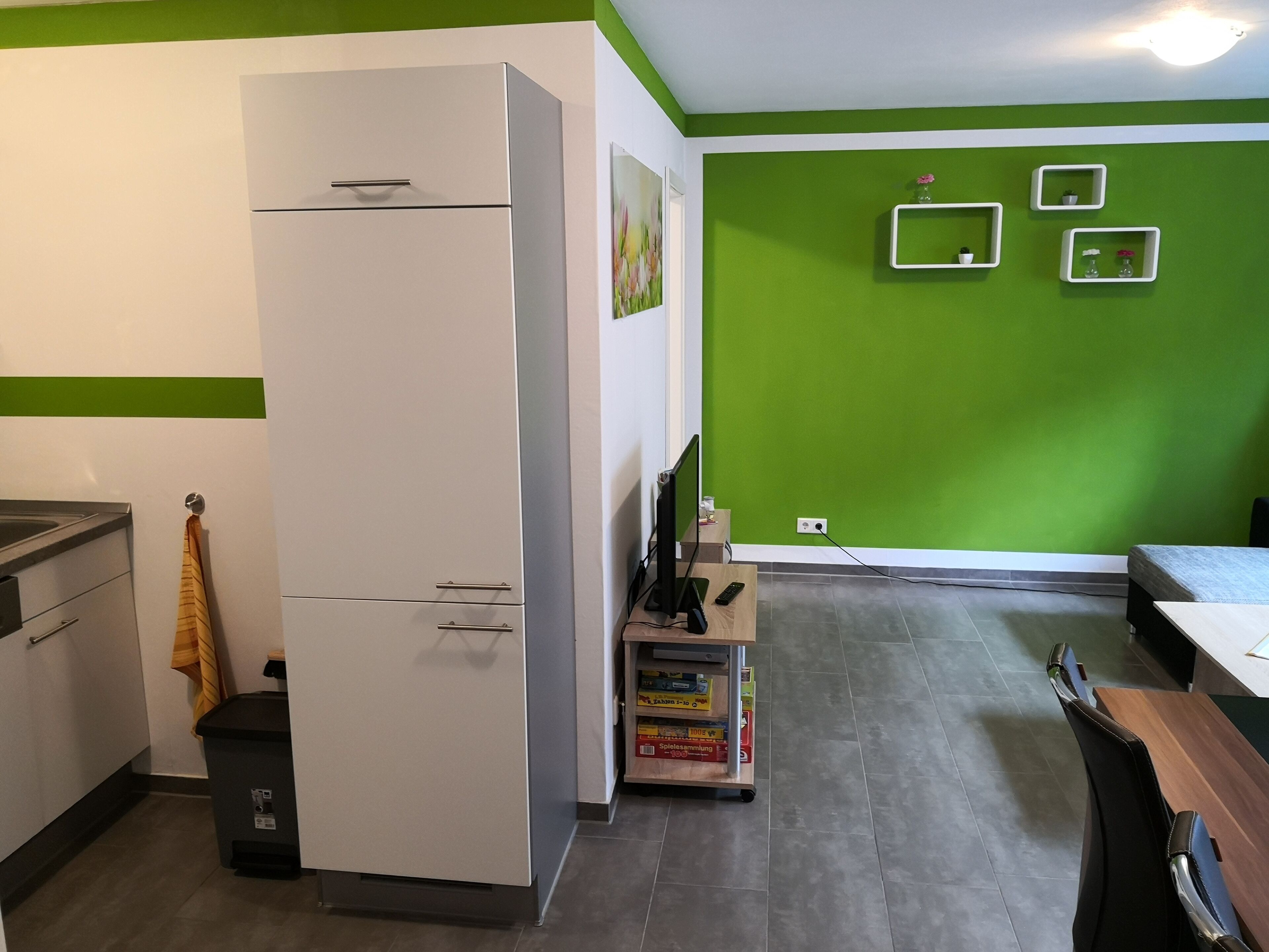 Een keuken met een witte koelkast, een houten tafel en een groene wand.