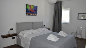Une chambre moderne avec un grand lit, un tableau coloré au mur, une table de chevet avec une lampe et une fenêtre avec des rideaux.