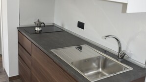 Une cuisine compacte dotée d’un évier en acier inoxydable, de meubles de rangement en bois foncé et d’un petit plan de travail.
