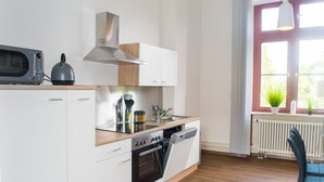 Een moderne keuken met witte kasten, een inbouwoven, een magnetron en een afzuigkap. Er is een raam met uitzicht op groen.