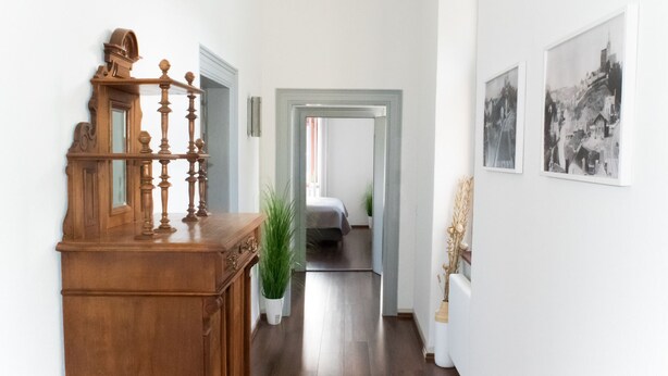 Een hal met een houten trap, een bed op de achtergrond en zwart-witfoto's aan de wanden.