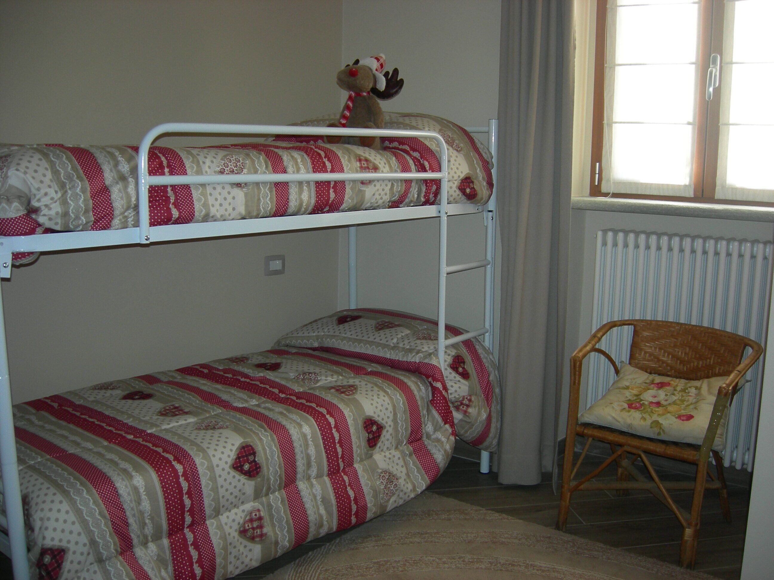 Un lit superposé avec une literie à motifs, une chaise avec un coussin à fleurs et une fenêtre avec des rideaux.