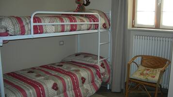 Un lit superposé avec une literie à motifs, une chaise avec un coussin à fleurs et une fenêtre avec des rideaux.
