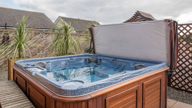 Een hottub met houten frame en afdekking, omringd door een houten terras en planten.