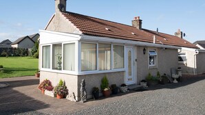Een gelijkvloers huis met een tuinkamer, een pannendak en een grindpad.