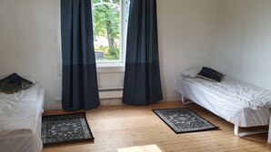 Quarto com duas camas de solteiro, um sofá branco e uma janela com cortinas escuras.