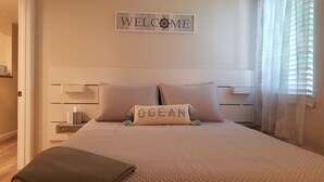 A bedroom with a bed, pillows, a bedside table, a tissue box, and a welcome sign on the wall. - Private Basement Suite Near Rehoboth & Lewes (Rehoboth Beach)