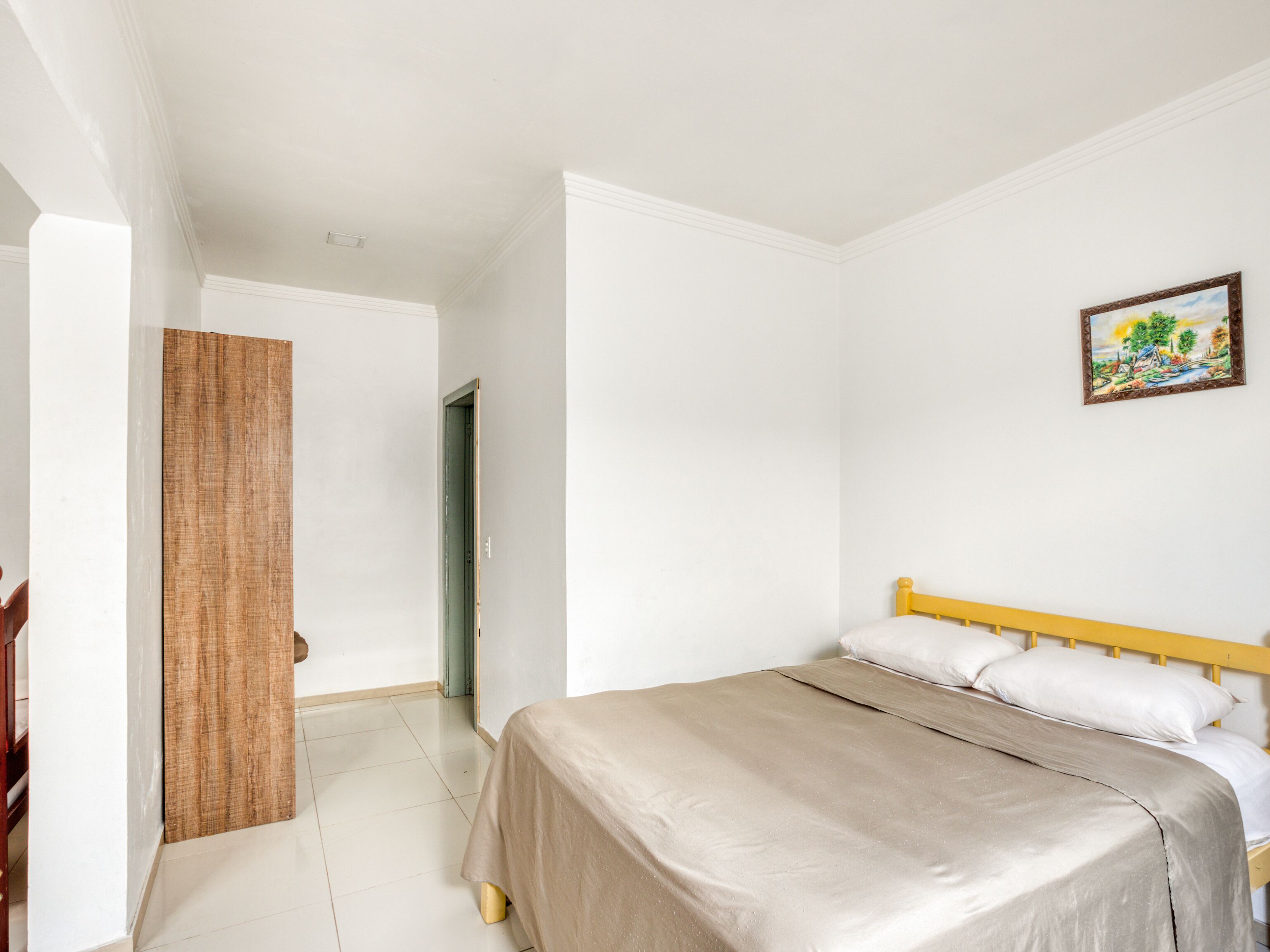 Quarto com cama, porta de madeira e um quadro na parede.