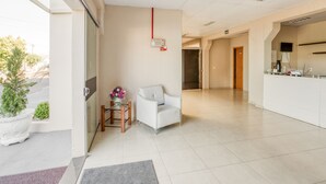 A clean, modern reception area with a reception desk, a seating area with a chair, and a small table with a vase of flowers. - Hotel Traveling (Passo Fundo)