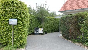 Ein Weg führt zu einem Gebäude mit roten Ziegeln auf dem Dach, umgeben von ordentlich geschnittenen Hecken.