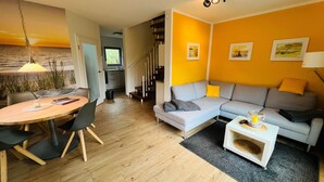 Ein modernes Wohnzimmer mit einem grauen Sofa, einem Esstisch mit Stühlen und einer Küche im Hintergrund.